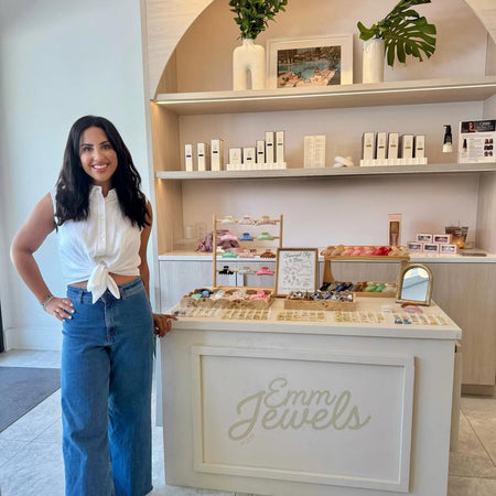 Emily Safran standing next to a jewelry display with 'Emm Jewels' branding.