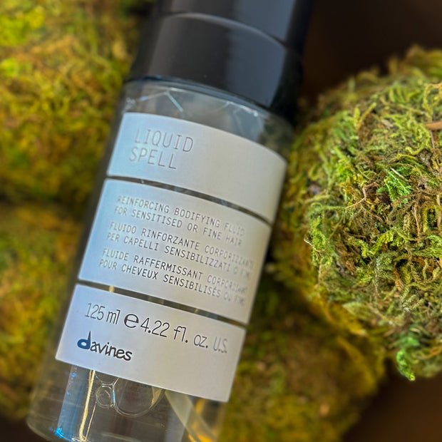 Bottle of Davines Liquid Spell on a textured green background