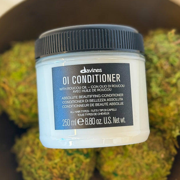 Davines OI Conditioner jar with text on a blurred green background