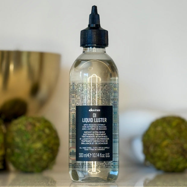 Bottle of davines Liquid Luster on a neutral background with decorative elements.