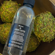 Davines Liquid Luster bottle with green spherical objects in the background