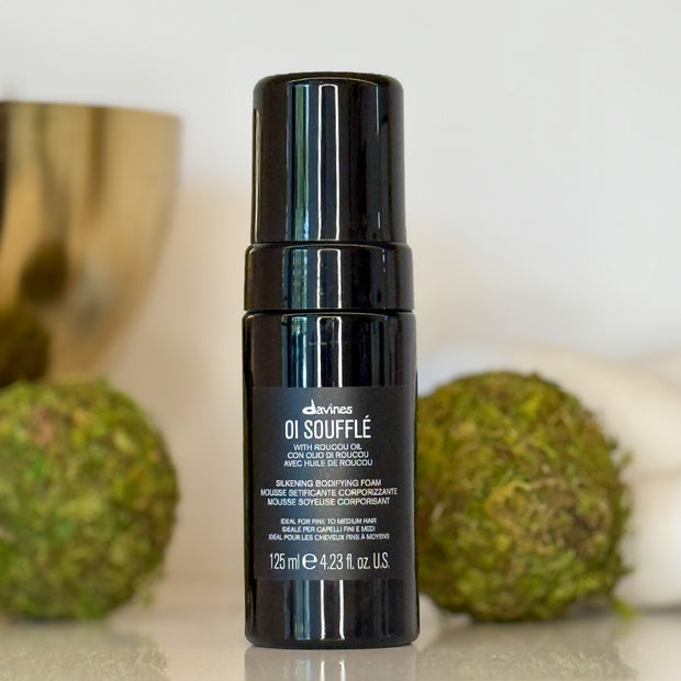 Black bottle of Davines OI Souffle hair product with green spherical objects in the background