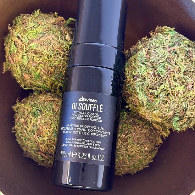 Davines OI Souffle hair product bottle on a background of green moss balls